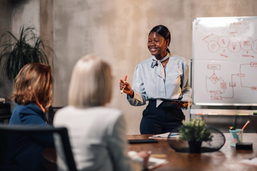 A professional woman guiding a discussion with colleagues at a whiteboard, representing employee empowerment through clarity and leadership.