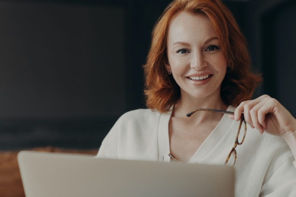 A professional woman smiling while working at a laptop, representing confident and approachable leadership.
