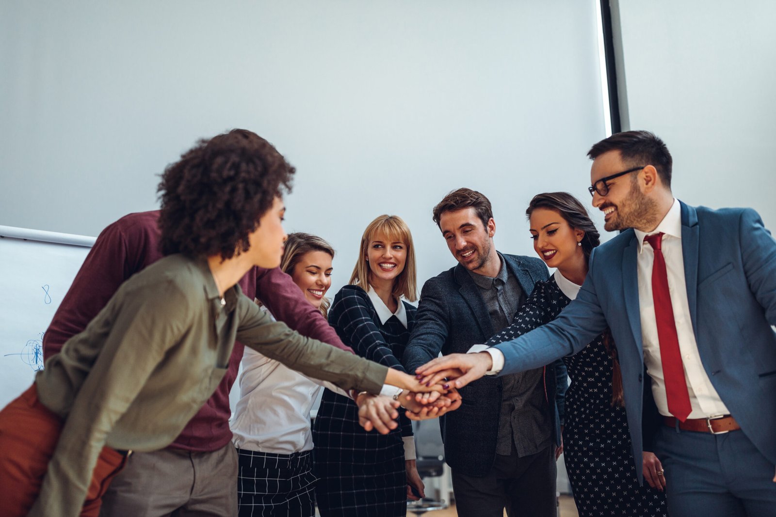 A diverse group of professionals placing their hands together, representing belonging, inclusion, and shared engagement at work.