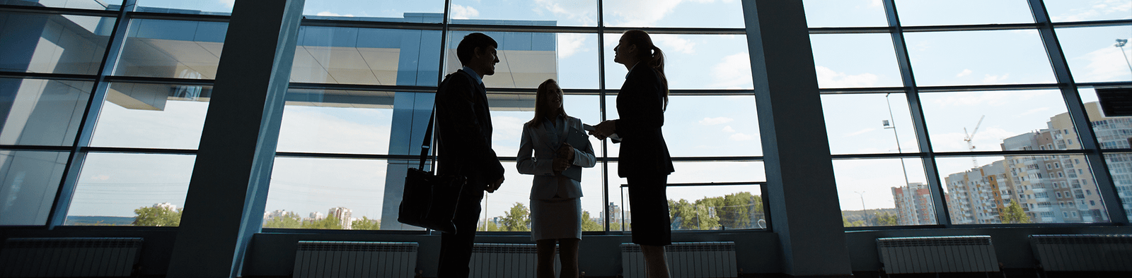 Three professionals standing and talking together in a workplace setting, representing a serious work-related conversation.