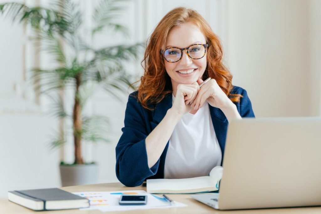 A professional woman smiling while seated at a desk with a laptop, representing confidence and emotional intelligence at work.