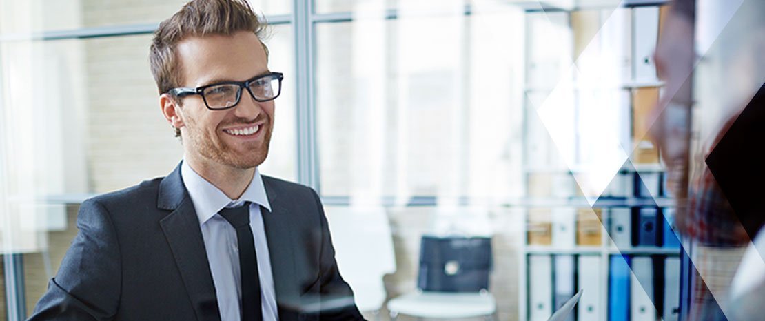 A professional man smiling during a conversation in an office setting, representing confidence in a job interview.
