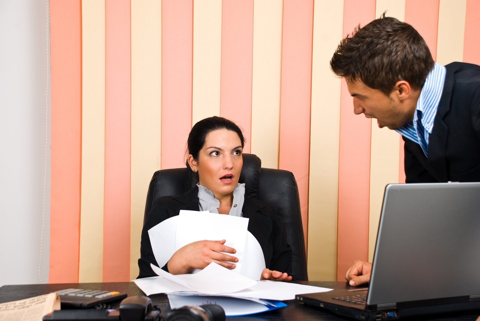 Woman looking uncomfortable as male colleague leans over her desk in an aggressive workplace interaction
