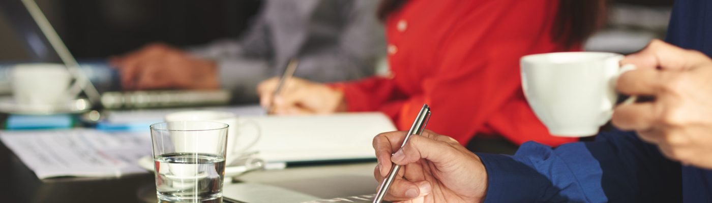 Close-up image of businessman drinking coffee and taking notes during the meeting
